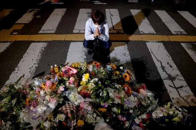 A person prays next to flowers laid at the site where late former Japanese Prime Minister Shinzo Abe was shot while campaigning for a parliamentary election, near Yamato-Saidaiji station in Nara, western Japan, July 8, 2022. (Photo by Issei Kato/Reuters)