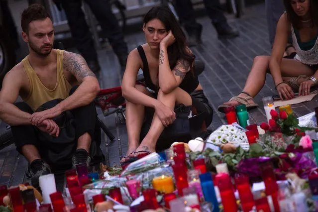 People sit next to candles and flowers placed on the ground after a terror attack that killed 14 people and wounded over 120 in Barcelona, Spain, Sunday, August 20, 2017. (Photo by Emilio Morenatti/AP Photo)