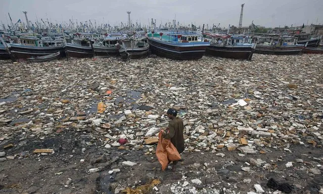 A boy looks to collect recyclable items through polluted waters in front of fishing boats at Karachi Fish Harbour August 6, 2014. (Photo by Akhtar Soomro/Reuters)