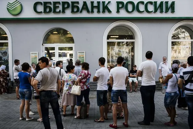 People stand in a queue to get into a branch of Sberbank of Russia bank in Donetsk on August 9, 2014. The centre of the one-million strong city appears to have become a new battleground in the fighting, coming under sustained shelling for the first time on August 7, with mortar fire hitting a hospital and residences near a key rebel base. (Photo by Dimitar Dilkoff/AFP Photo)