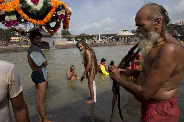 An Indian Sadhu, or Hindu holy man, right, dries his hair after a bath as others take a bath in the Godavari River during Kumbh Mela, or Pitcher Festival, in Nashik, India, Saturday,  August 29, 2015. (Photo by Tsering Topgyal/AP Photo)