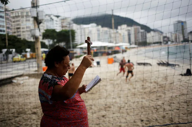 A woman prays next to people playing volleyball on Copacabana beach in Rio de Janeiro, Brazil, June 4, 2016. (Photo by Nacho Doce/Reuters)