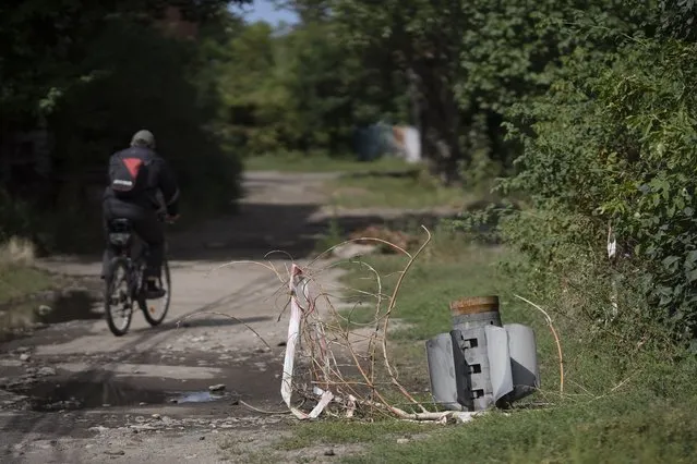 A man cycles past part of a rocket that sits wedged in the ground at a residential area in Sloviansk, Ukraine, Monday, September 5, 2022. (Photo by Leo Correa/AP Photo)