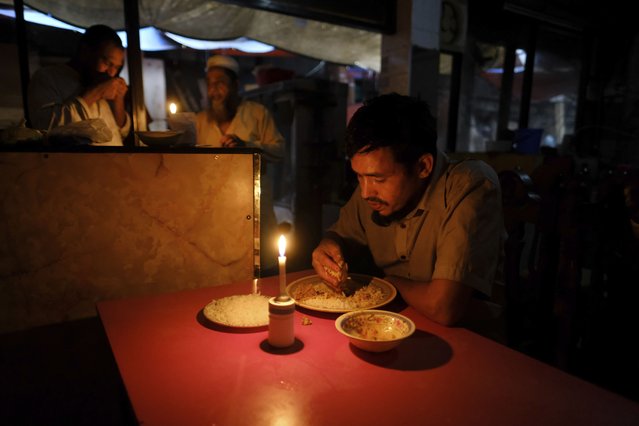 A person eats in a restaurant under candle lights during a power failure in Dhaka, Bangladesh. October 4, 2022. A failure in Bangladesh's national power supply grid plunged most of the country into a blackout on Tuesday, officials said. (Photo by Mahmud Hossain Opu/AP Photo)