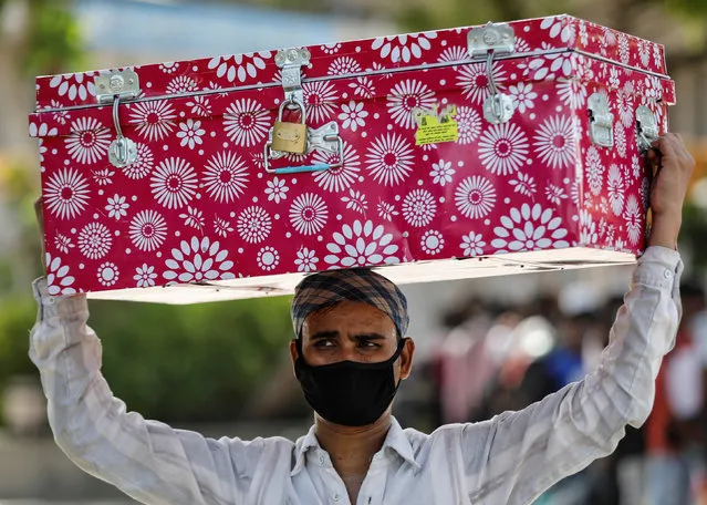 A migrant worker carries a luggage trunk on his head as he waits for transport to reach a railway station to board a train to his home state of Bihar, during an extended lockdown to slow the spreading of the coronavirus disease (COVID-19), in Ahmedabad, India, May 23, 2020. (Photo by Amit Dave/Reuters)