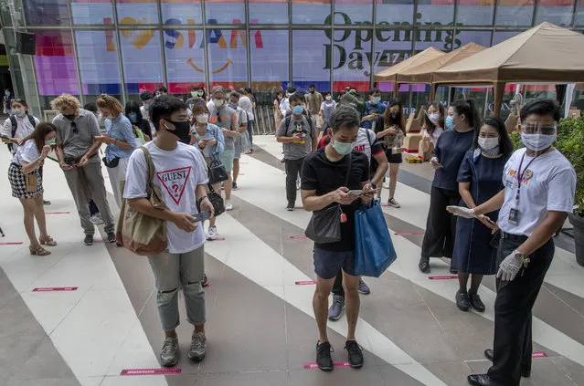 Patrons stand maintaining a physical distance at the entrance of the upmarket shopping mall Siam Paragon in Bangkok, Thailand, Sunday, May 17, 2020. Thai authorities allowed department stores, shopping malls and other businesses to reopen from Sunday, selectively easing restrictions meant to combat the coronavirus. (Photo by Gemunu Amarasinghe/AP Photo)