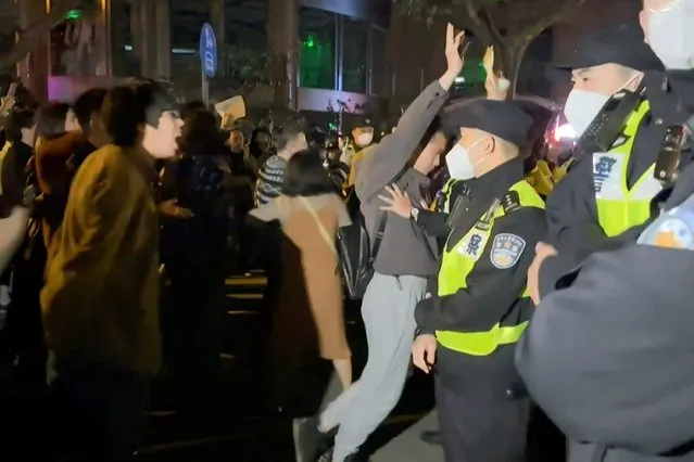 This frame grab from eyewitness video footage made available via AFPTV on November 27, 2022 shows demonstrators shouting slogans as police hold their positions, in Shanghai. - Angry crowds took to the streets in Shanghai in the early hours of November 27 and videos on social media showed protests in other cities across China, as public opposition to the government's hardline zero-Covid policy mounts. (Photo by AFPTV/AFP Photo)