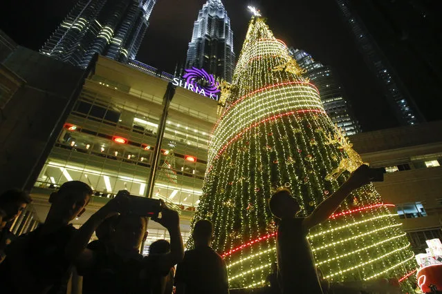 Tourists take selfies in front of a Christmas tree at the Petronas Twin Towers in Kuala Lumpur, Malaysia, Wednesday, December 13, 2017. Shopping malls in the Muslim-dominated nation have been decorated with Christmas trees, Santa Claus figures and illuminations to attract year-end shoppers. (Photo by Sadiq Asyraf/AP Photo)