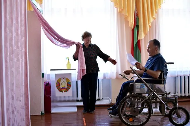 A woman assists a man in a wheelchair during early voting for Belarus' presidential election at a polling station in the village of Proshkava, some 180 km north of Minsk, on August 4, 2020. (Photo by Sergei Gapon/AFP Photo)