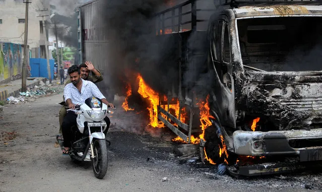 Men ride a motorcycle past a lorry in Bengaluru, which was set on fire by protesters after India's Supreme Court ordered Karnataka state to release 12,000 cubic feet of water per second every day from the Cauvery river to neighbouring Tamil Nadu, India September 12, 2016. (Photo by Abhishek N. Chinnappa/Reuters)