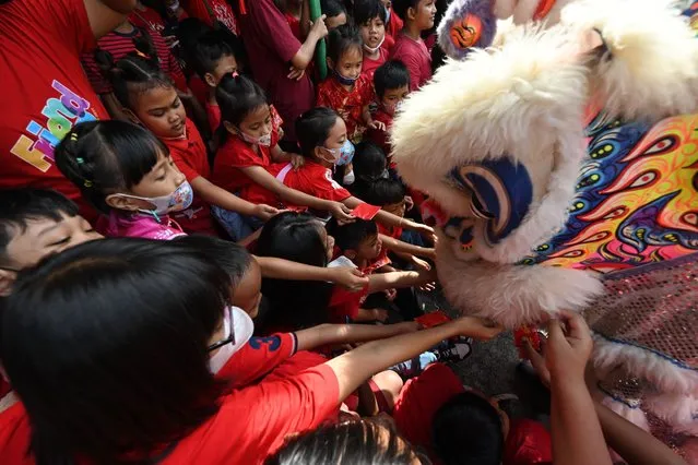 Children give money to lion dance performers at a school as part of festivities to welcome the upcoming Lunar New Year of the Rabbit in Solo, Central Java on January 19, 2023. (Photo by Adek Berry/AFP Photo)