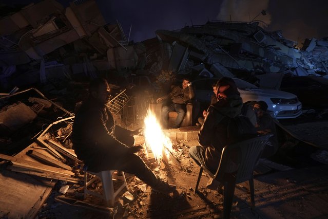 People warm up with fire in front of destroyed buildings in Antakya, southern Turkey, Wednesday, February 8, 2023. With the hope of finding survivors fading, stretched rescue teams in Turkey and Syria searched Wednesday for signs of life in the rubble of thousands of buildings toppled by a catastrophic earthquake. (Photo by Khalil Hamra/AP Photo)