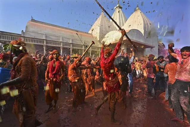 Men from Barsana village smeared with colors play Holi at Nandagram temple in Nandgoan village, 115 kilometers (70 miles) south of New Delhi, India, Wednesday, March 1, 2023. Women from Nandgaon, the birthplace of Hindu God Krishna, beat the men from Barsana, the legendary birthplace of Radha, the consort of Krishna, with wooden sticks in response to their efforts to put color on them. The same act is then replicated in Barsana between the women of that village and the men of Nandgaon as they observe the Lathmar Holi festival, a celebration of love and friendship. (Photo by Deepanshu Aggarwal/AP Photo)