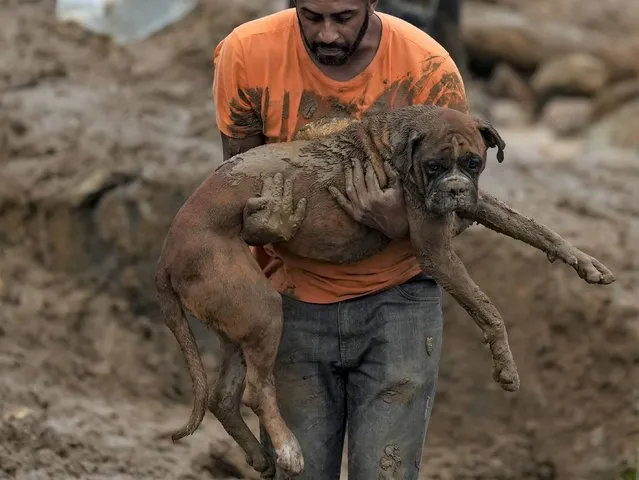 A man carries a dog away from a residential area destroyed by mudslides in Petropolis, Brazil, Wednesday, February 16, 2022. Extremely heavy rains set off mudslides and floods in a mountainous region of Rio de Janeiro state, killing multiple people, authorities reported. (Photo by Silvia Izquierdo/AP Photo)