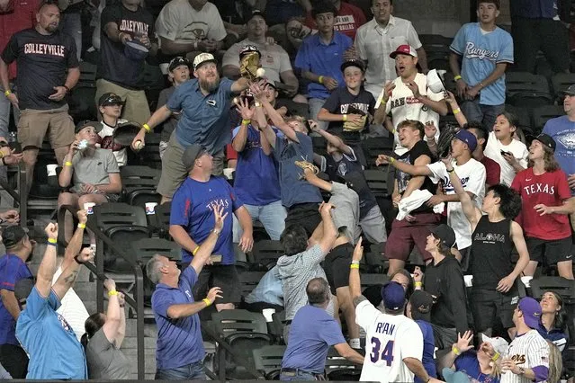 Fans reach out trying to catch a grand slam ball hit by Texas Rangers' Adolis Garcia in the sixth inning of a baseball game against the Kansas City Royals, April 10, 2023, in Arlington, Texas. (Photo by Tony Gutierrez/AP Photo)