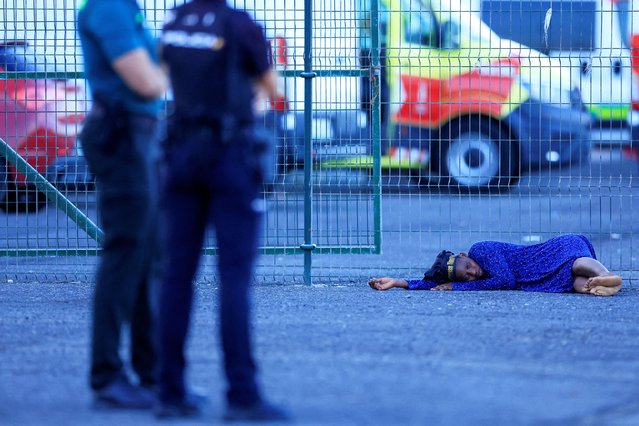 A woman lies on the ground while waiting to be treated by the Red Cross after disembarking from a Spanish coast guard vessel, in the port of Arguineguin, on the island of Gran Canaria, Spain on October 20, 2024. (Photo by Borja Suarez/Reuters)
