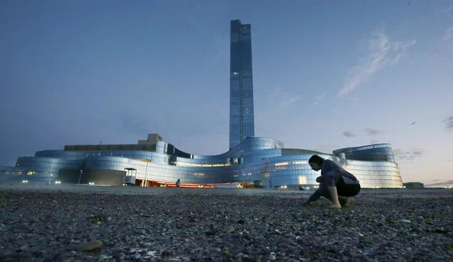 Paula Manago, of Cliffside Park, N.J., gathers shells along the ocean near the Revel Hotel Casino early Tuesday, September 2, 2014, in Atlantic City, N.J. The casino section of the Revel closed at 6:30 a.m. Tuesday. Revel is shutting down a little over two years after opening with high hopes of revitalizing Atlantic City's struggling gambling market. (Photo by Mel Evans/AP Photo)