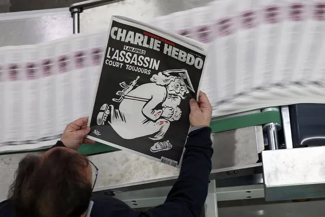 An employee of a printing house holds a copy of the latest edition of French weekly newspaper Charlie Hebdo with the title "One year on, The assassin still on the run" near Paris, France, January 4, 2016. France this week commemorates the victims of last year's Islamist militant attacks on satirical weekly Charlie Hebdo and a Jewish supermarket with eulogies, memorial plaques and another cartoon lampooning religion. (Photo by Benoit Tessier/Reuters)