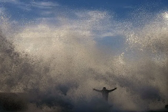 A person stands as a wave crashes against the sea defenses at the promenade of the beach in Rabat, Morocco, Thursday, February 9, 2023. (Photo by Manu Fernandez/AP Photo)