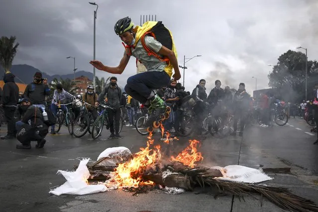 An anti-government demonstrator in skates jumps over a fire during a protest in Bogota, Colombia, Wednesday, May 5, 2021. The protests that began last week over a tax reform proposal continue despite President Ivan Duque's withdrawal of the tax plan on Sunday, May 2. (Photo by Ivan Valencia/AP Photo)