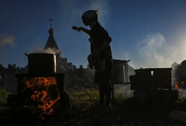 A woman cooks a meal during a pilgrimage of Orthodox believers, who celebrate the icon of St. Nicholas in the village of Bobino in Kirov Region, Russia on June 3, 2021. (Photo by Alexey Malgavko/Reuters)