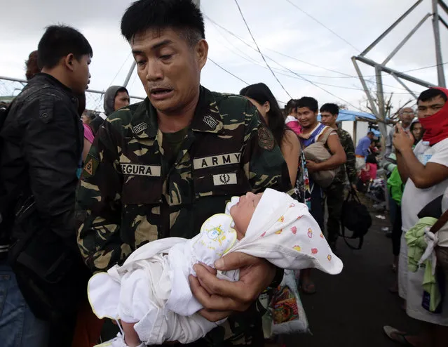 A soldier carries one-day-old baby Ian Daniel Honrado to a waiting military transport plane Wednesday November 13, 2013 from the damaged Tacloban airport  at Tacloban city, Leyte province in central Philippines. (Photo by Bullit Marquez/AP Photo)