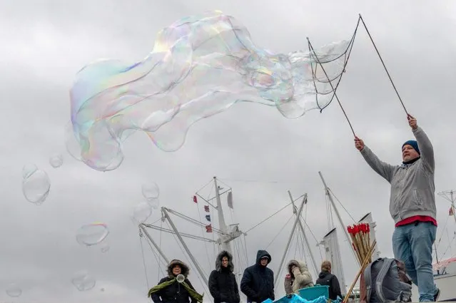 A street artist makes soap bubbles against the backdrop of the harbor in rainy weather in Hamburg, Germany, December 25, 2016. (Photo by Axel Heimken/EPA)