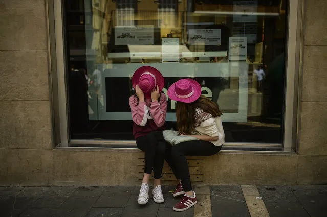 Women wearing rose color hats cover their faces during a wine-tasting on the street to promote Spanish wine on a sunny spring day, in Pamplona northern Spain, on Saturday, May 19, 2018. Spanish rose wine is a typical wine of this region of Spain. (Photo by Alvaro Barrientos/AP Photo)