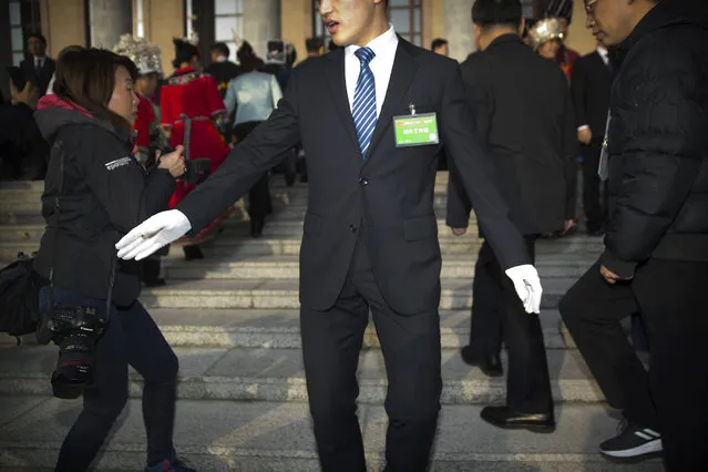 In this Tuesday, March 5, 2019 photo, a security official tries to keep journalists back from the steps of the Great Hall of the People as delegates arrive for the opening session of China's National People's Congress (NPC) in Beijing. The annual meeting of China's legislature is a highly scripted affair, but quirky moments and offbeat details lurk around the edges and behind the scenes. (Photo by Mark Schiefelbein/AP Photo)