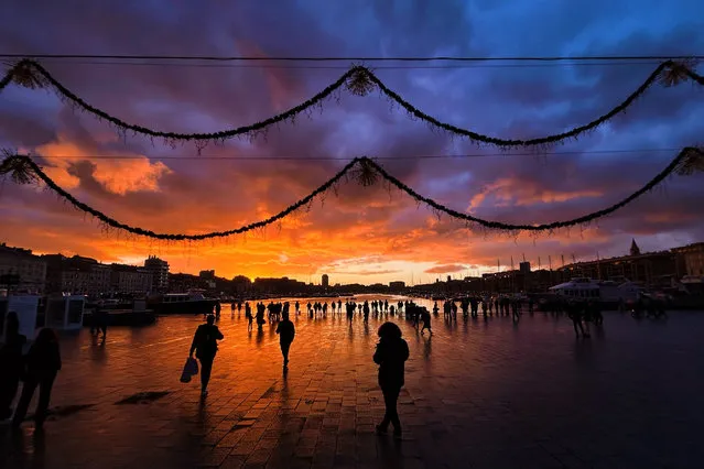 People walk along the Vieux-Port (the Old Port) at sunset in Marseille, southern France, on December 4, 2023. (Photo by Nicolas Tucat/AFP Photo)