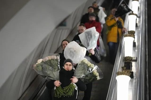 A man goes down the escalator in the subway holding bunches of flowers purchased from the flower market on International Women's Day, in Moscow, Russia, early Friday, March 8, 2024. International Women's Day on March 8 is an official holiday in Russia. Per tradition, men give flowers and gifts to female relatives, friends and colleagues, even though in the past two years flowers have gotten more expensive. (Photo by Alexander Zemlianichenko/AP Photo)