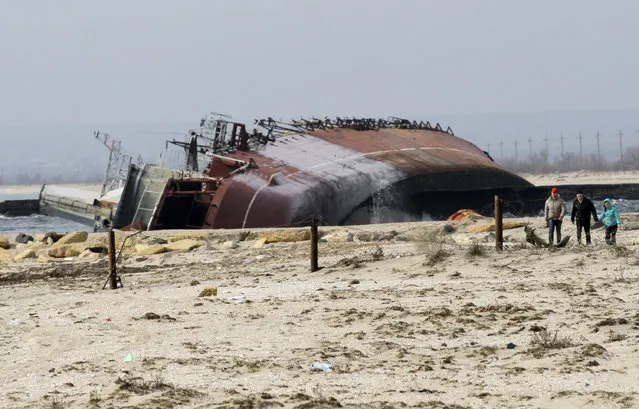 People walk past the scuttled decommissioned Russian vessel “Ochakov” on the Black Sea shore outside the town of Myrnyi, western Crimea, Ukraine, Thursday, March 6, 2014.  In the early hours of Thursday Russian naval personnel scuttled the decommissioned ship, blockading access for five Ukrainian Naval vessels now trapped inside of the Southern Naval Headquarters located in Myrnyi in Western Crimea as Russian war vessels patrolled just of the coast. (Photo by Darko Vojinovic/AP Photo)