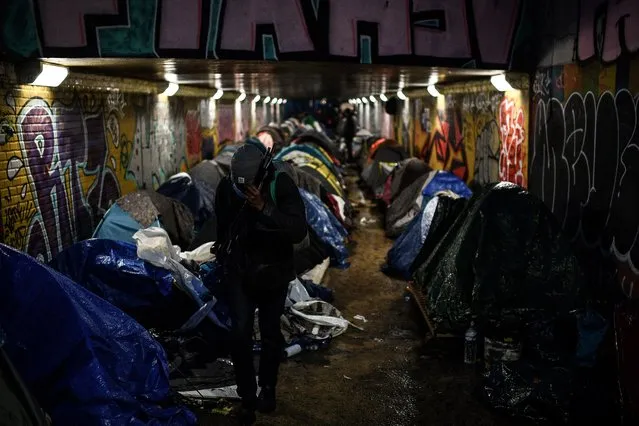 A migrant carries his belongings at a makeshift camp set up under a pedestrian tunnel passing underneath the ring road during an evacuation operation between Paris and the northeastern suburb of Le Pre Saint Gervais early on December 10, 2021. (Photo by Christophe Archambault/AFP Photo)