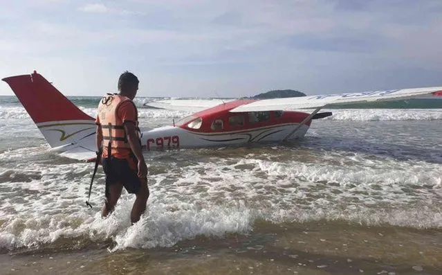 In this handout photo provided by the Philippine Coast Guard District Palawan, a rescuer walks beside a Cessna 206 plane carrying two pilots and 25 boxes of live fish after it crash-landed Friday December 10, 2021, on the shoreline near the resort town of El Nido in western Palawan province, Philippines, due to engine trouble, civil aviation officials said. Philippine coast guard personnel rescued the two pilots from the floating aircraft near the beach, where the private plane ditched after taking off from San Vicente town in Palawan on a domestic flight to Sangley airport in Cavite province south of Manila. (Photo by Philippine Coast Guard District Palawan via AP Photo)