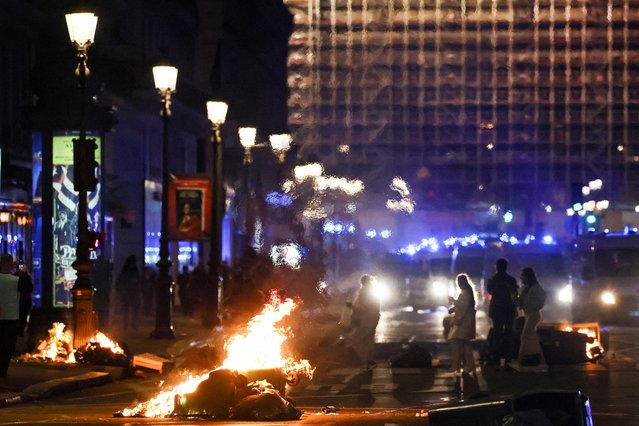 People walk past burning garbage bins near the Opera Garnier on the day the National Assembly debates and votes on two motions of no-confidence against the French government, tabled by centrist group Liot and far-right Rassemblement National party, for its use of article 49.3, a special clause in the French Constitution, to push the pensions reform bill through the National Assembly without a vote by lawmakers, in Paris, France on March 20, 2023. (Photo by Yves Herman/Reuters)