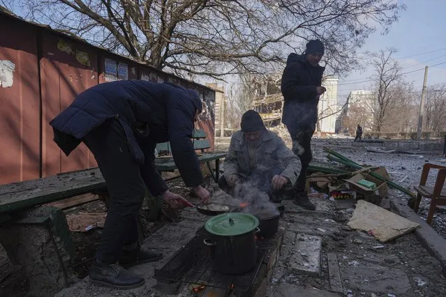 Men cook a meal in a street in Mariupol, Ukraine, Sunday, March 13, 2022. (Photo by Evgeniy Maloletka/AP Photo)