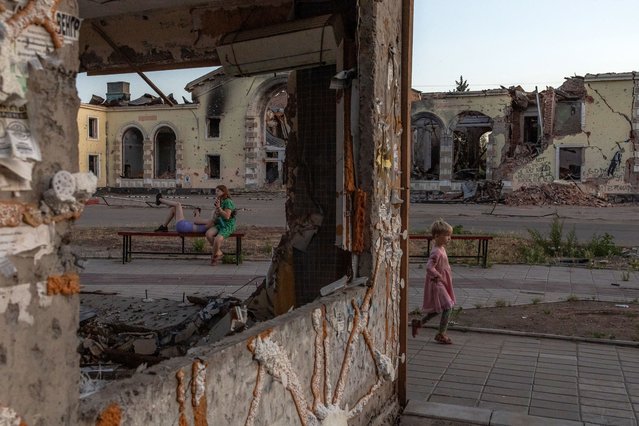 A child plays as women rest on a bench in front of destroyed by shelling residential buildings in Kostyantynivka, the eastern Donetsk region, on June 22, 2024, amid the Russian invasion of Ukraine. (Photo by Roman Pilipey/AFP Photo)