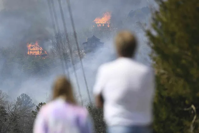 People watch as structures burn from a wildfire Wednesday, March 30, 2022, in Sevierville, Tenn. Firefighters sought to get a handle Wednesday on a wildfire spreading near Great Smoky Mountains National Park in Tennessee, amid mandatory evacuations as winds whipped up ahead of a line of strong storms forecast to move in overnight. (Photo by Caitie McMekin/Knoxville News Sentinel via AP Photo)