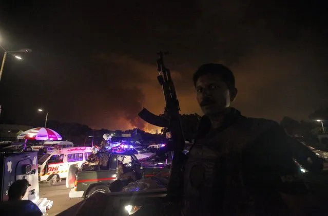 A policeman with a gun stands guard on a vehicle as smoke billows from Jinnah International Airport in Karachi, June 9, 2014. REUTERS/Athar Hussain