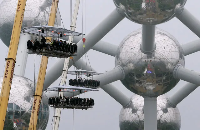 Three of the ten tables, accommodating a total of 220 guests, are suspended from a crane at a height of 40 metres in front of the Atomium, a 102-metre (335 feet) high structure and its nine spheres, built for the 1958 Brussels World's Fair, as part of the 10th anniversary of the event known as “Dinner in the Sky”, in Brussels, Belgium June 1, 2016. (Photo by Yves Herman/Reuters)