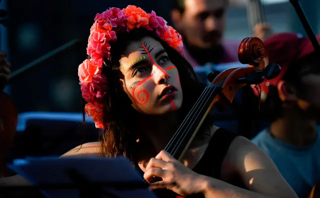 A musician with her face painted as an indigenous performs during a concert in honor of the indigenous guards of Colombia, in Bogota on December 5, 2019. Indigenous guards who arrived Bogotá to join the protests against President Iván Duque were honored by a student orchestra in the middle of another failed meeting between the government and the promoters of the mobilizations, which add up to 15 days although this Thursday the participation was narrowed. (Photo by Juan Barreto/AFP Photo)