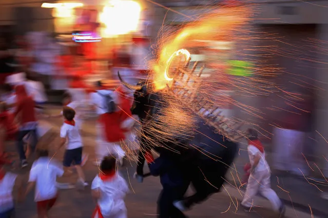 People and children are chased by a Toro del Fuego (flaming bull) as it is runs through the streets of Pamplona on the third day of the San Fermin Running Of The Bulls Festival  on July 8, 2014 in Pamplona, Spain. The annual Fiesta de San Fermin, made famous by the 1926 novel of US writer Ernest Hemmingway “The Sun Also Rises”, involves the running of the bulls through the historic heart of Pamplona. (Photo by Christopher Furlong/Getty Images)