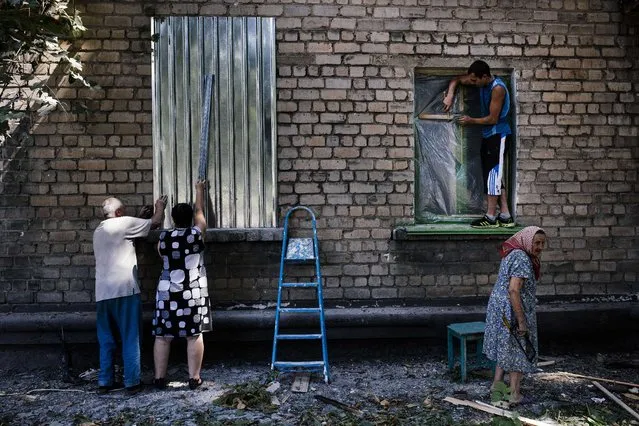 People fix their broken windows after shelling in Donetsk on August 9, 2014. The centre of the one-million strong city appears to have become a new battleground in the fighting, coming under sustained shelling for the first time on August 7, with mortar fire hitting a hospital and residences near a key rebel base. Ukraine said on August 8 it warded off a Russian attempt to send troops across the border under the guise of a humanitarian mission, fuelling Western fears that Moscow is planning to invade. (Photo by Dimitar Dilkoff/AFP Photo)