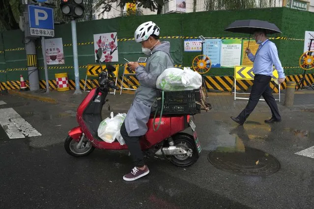 A delivery man checks his phone during a rainy day in Beijing, Thursday, August 18, 2022. Some were killed with others missing after a flash flood in western China Thursday, as China faces both summer rains and severe heat and drought in different parts of the country. (Photo by Ng Han Guan/AP Photo)