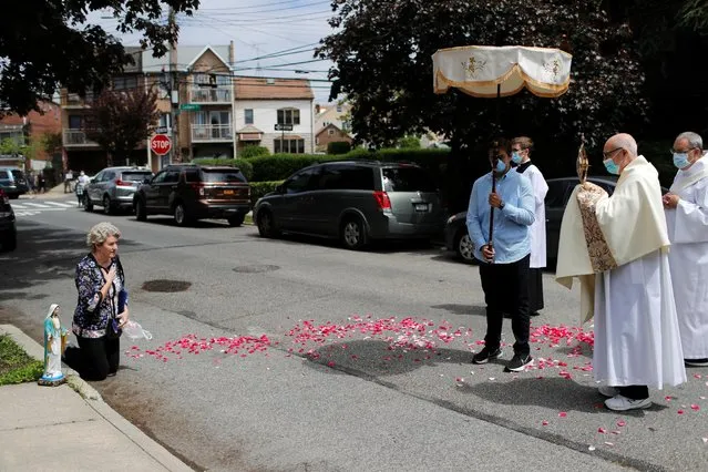 Deacon Robert Lavanco of Our Lady of Hope Catholic Church, prays with Krystyna Kopacki as she kneels in the street during a procession called the Blessed Sacrament, to bring blessings to worshippers outside their homes while their church sanctuary is closed to them in the Queens borough of New York City, New York, U.S., May 24, 2020. (Photo by Mike Segar/Reuters)