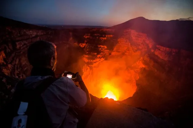 A tourist takes pictures of a lava lake inside the crater of the Masaya Volcano in Masaya, some 30km from Managua on May 19, 2016. Hundreds of tourists arrive daily to observe the lava flow which formed six months ago near the surface of the crater of the small Masaya volcano, one of the most active in Nicaragua. (Photo by Inti Ocon/AFP Photo)