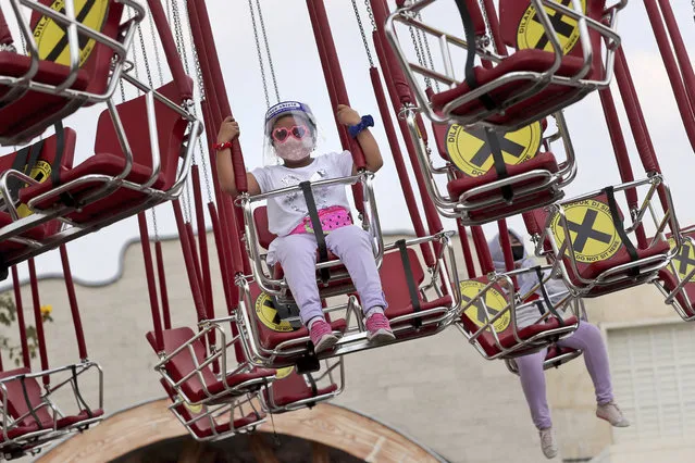 A young girl wearing a protective face shield enjoys a swing ride as physical distancing markings are seen on the seats during the first day of the reopening of Dunia Fantasi Amusement Park after weeks of closure due to the large-scale restrictions imposed to help curb the new coronavirus outbreak, at Ancol Dream Park in Jakarta, Indonesia, Saturday, June 20, 2020. (Photo by Tatan Syuflana/AP Photo)