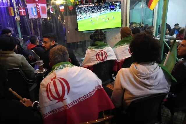 Lebanese soccer fans of Iran's team cover their backs with Iranian flags, as they sit at a coffee shop smoking water pipes and watch the World Cup group B soccer match between Iran and the United States, in the Hezbollah stronghold in the southern suburbs of Beirut, Lebanon, Tuesday, November 29, 2022. (Photo by Hussein Malla/AP Photo)