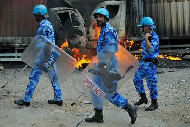 Members of the security forces make their way past burning lorries in Bengaluru, which were set on fire by protesters after India's Supreme Court ordered Karnataka state to release 12,000 cubic feet of water per second every day from the Cauvery river to neighbouring Tamil Nadu, India September 12, 2016. (Photo by Abhishek N. Chinnappa/Reuters)