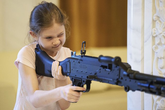 A girl holds a firearm at an exhibition inside Romania's Palace of Parliament during a series of events marking International Children's Day in Bucharest, Romania, Sunday, June 1, 2025. (Photo by Andreea Alexandru/AP Photo)